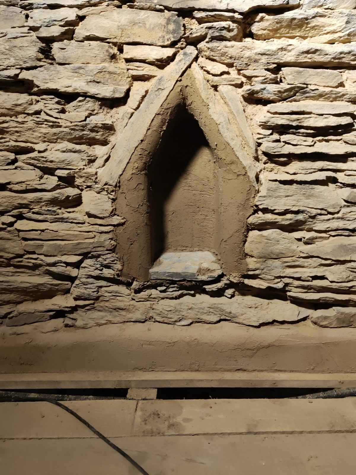 Historisches Bruchsteinmauerwerk mit spitzbogiger Nische innen, von oben beleuchtet