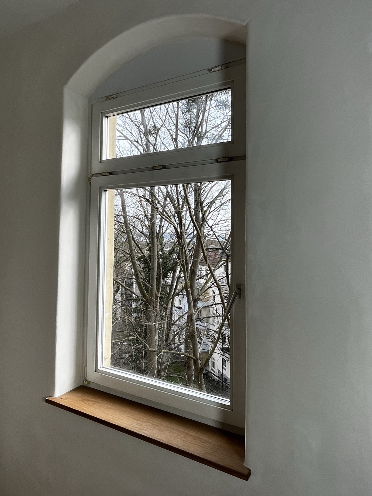 Sanierter Altbau-Raum: neugotisches Rundbogenfenster mit weißem Kalkputz eingerahmt