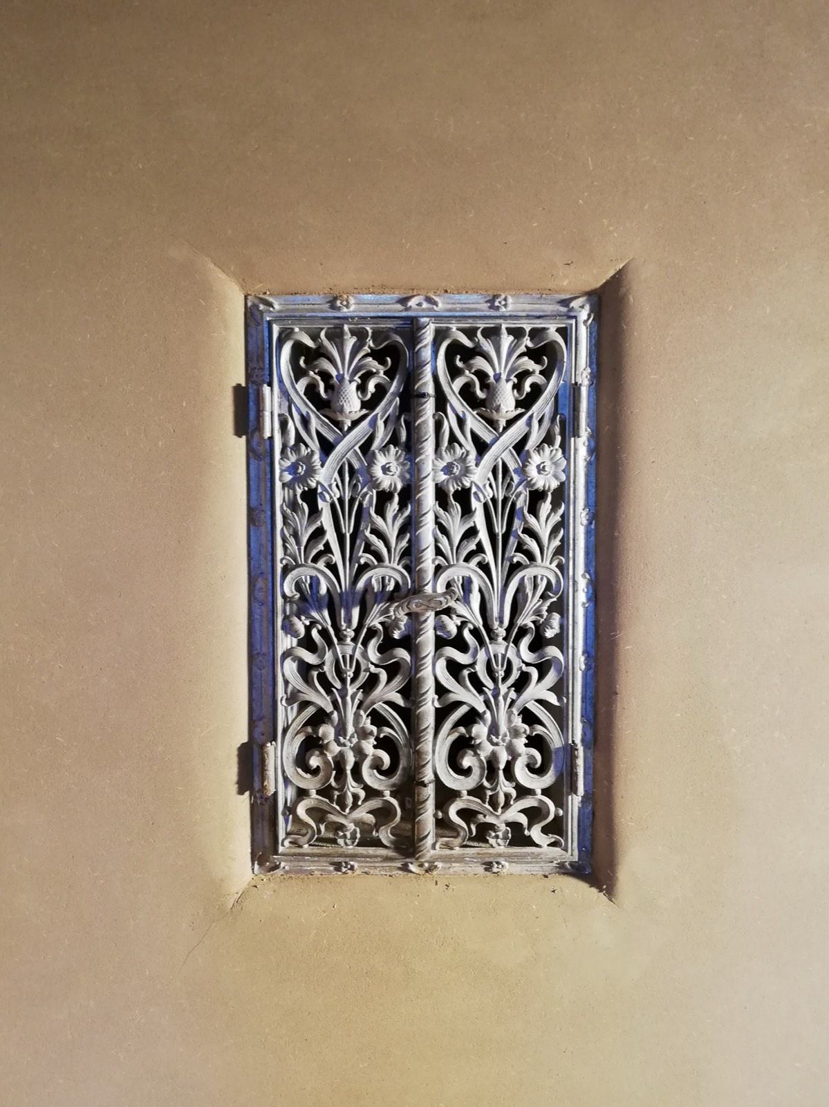 Schmiedeeisernes Fenster in Lehmputzwand: kunstvolles Gitter, Jugendstil-Ornamentik