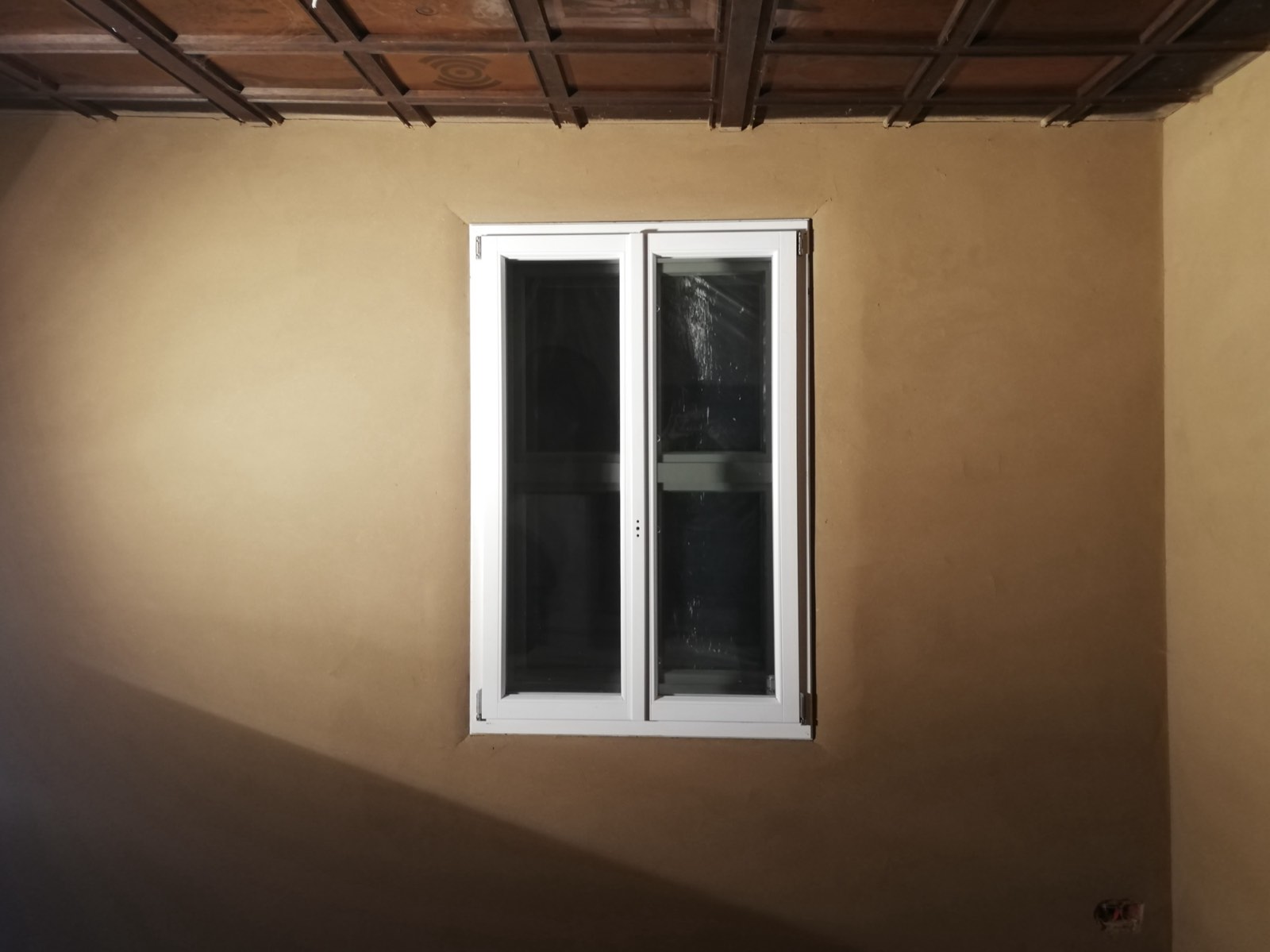 Lehmputzwand mit historischem Holzbalken und kleiner Fensteröffnung, Detailansicht