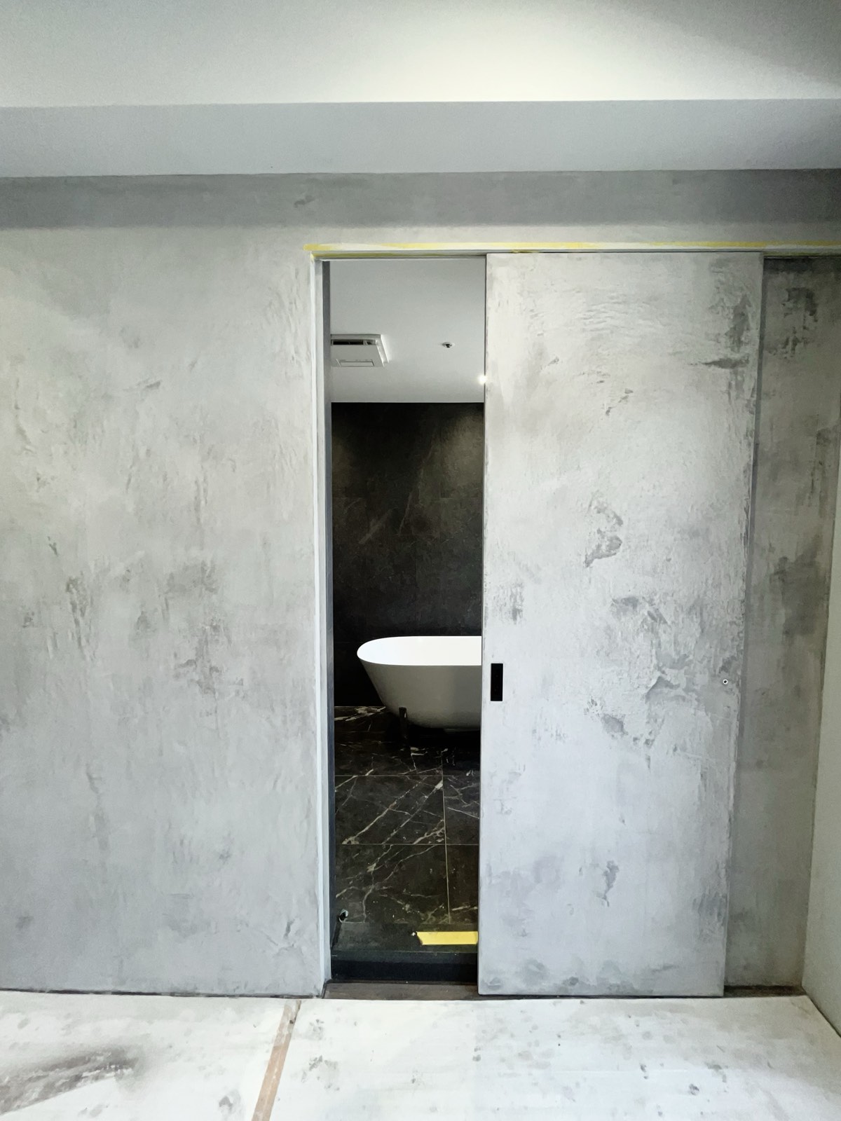Kalkputzwand mit Badtür: grau-weiße Oberfläche, freistehende Badewanne sichtbar